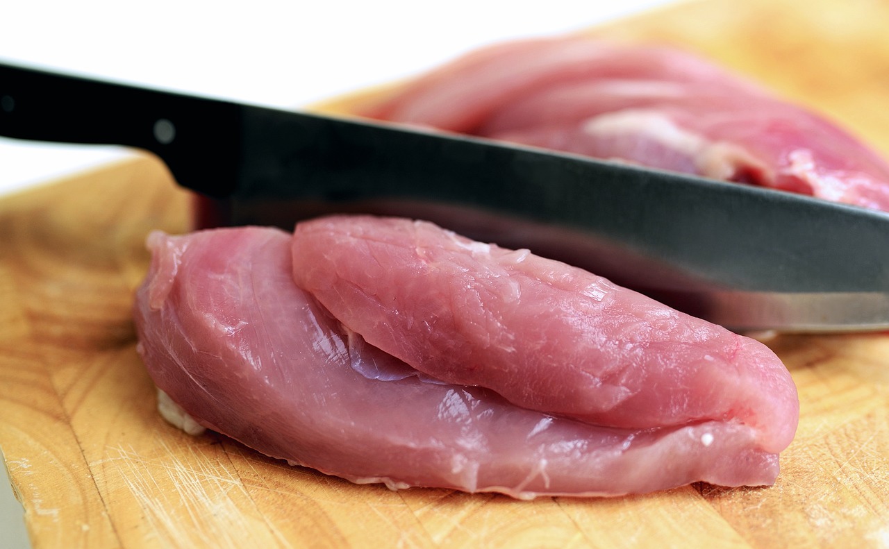 poultry meat being cut with a knife on a chopping board